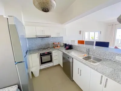a white kitchen with a sink and a refrigerator at Nayah Stays, Joubal Lagoons flowery apartment in Hurghada