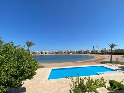 a swimming pool next to a beach with palm trees at Nayah Stays, Joubal Lagoons flowery apartment in Hurghada