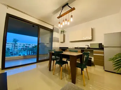 a kitchen with a table and chairs and a refrigerator at Sunny 1 BR Apt G cribs ElGouna with open View in Hurghada