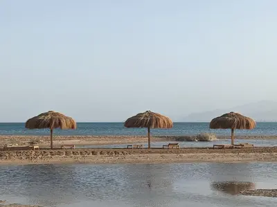 three straw umbrellas and benches on a beach at Modern Beachfront 1BR Loft with Garden in Somabay in Hurghada