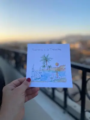 a person holding up a drawing of a beach at Appartement avec rooftop au cœur de Louxor vue sur le Nil in Jazīrat al ‘Awwāmīyah