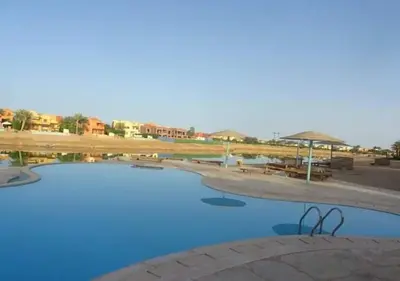 a swimming pool with blue water and tables and umbrellas at Warm One Bedroom at West Golf Y62 in Hurghada