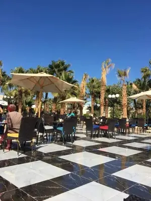 a patio with chairs and tables and umbrellas and palm trees at ميراج in Hurghada