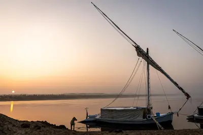 a man standing next to a boat on the beach at Nuba Tod Sailling boat in Aswan