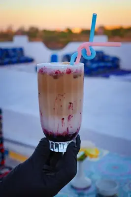 a person holding up a drink with a straw at Kulaih nubian guest house in Aswan
