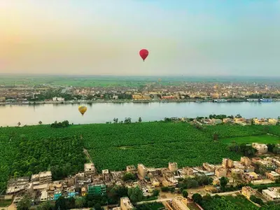 two hot air balloons flying over a river at Luxor in Luxor