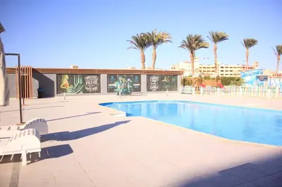 a pool with chairs and palm trees and a building at Scandic Hotel Hurghada in Hurghada
