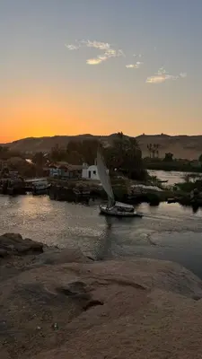 a boat with a sail on a river at sunset at Nubian Soul Guest Houses in Aswan