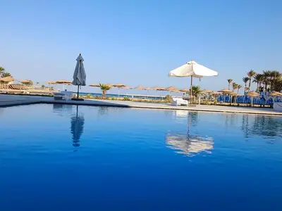 a swimming pool with an umbrella and chairs and umbrellas at Vitamin Sea, Beach Front Central Free Wi-Fi in Hurghada