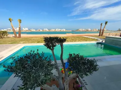 a swimming pool with palm trees in front of the beach at Stay at elgouna with private heated pool villa in Hurghada