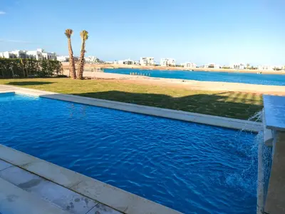 a swimming pool with blue water and palm trees at Ancient Sand villa at Elgouna with private heated pool in Hurghada