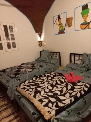 a bedroom with two beds and paintings on the wall at Mountain hug house in Luxor