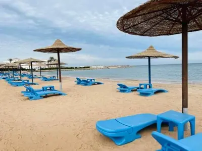 a beach with blue chairs and umbrellas and the ocean at Furnished Chalets for Rent in Cecilia Resort Furnteched, kitchenee, Near Airport in Hurghada