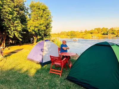 a man sitting at a table next to two tents at Anoosh camp in Aswan