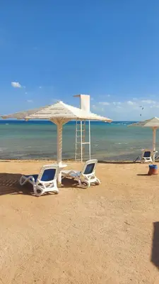 three lounge chairs and an umbrella on a beach at Selina Bay Resort in El Gouna