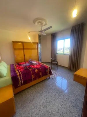 a bedroom with a bed and a chair and a window at Tonys Flat in Al Aqālitah