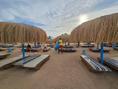 a beach with lounge chairs and straw umbrellas at Taiba Golden Central Hurghada in Hurghada