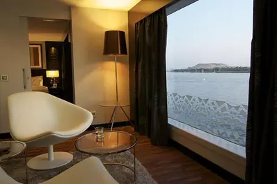 a room with a large window with a view of the water at King of The Vally Nile Cruise Aswan To Luxor 3 Night And visit the Nubian village in Aswan