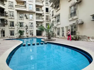 a woman stands next to a swimming pool in front of a building at Cleopatra Style City Center in Hurghada