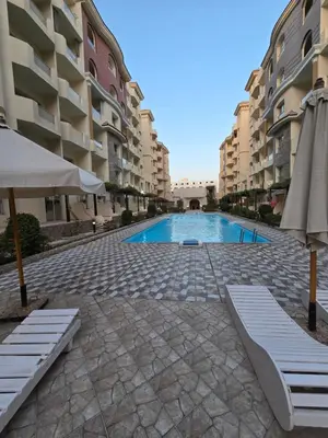 a swimming pool with two chairs and an umbrella and some buildings at Florenza khamsin Resort in Hurghada