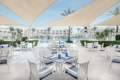 a restaurant with white tables and chairs and palm trees at JAZ Aquaviva in Hurghada