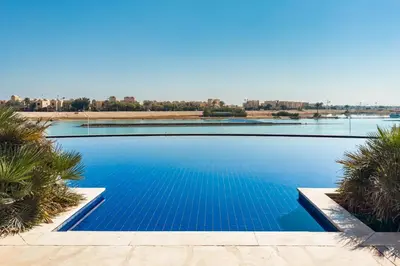 a swimming pool with blue water and palm trees at The 2BDR Warmhearted Waterside Apt in Hurghada