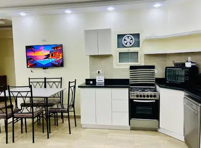 a kitchen with white cabinets and a stove and chairs at Beachfront Bliss - Your Hurghada Escape Awaits in Hurghada