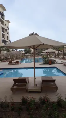 a pool with an umbrella and some chairs and a table at Amazing Apartment Aldau Heights in Hurghada