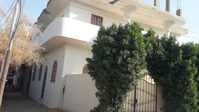 a white house with trees in front of a fence at الاقصر البر الغربي امام معبد هابو in Al Aqālitah