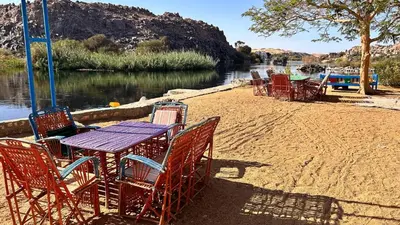 a table and chairs sitting on a beach next to a river at Cataract Nile View Rooms in Shellal