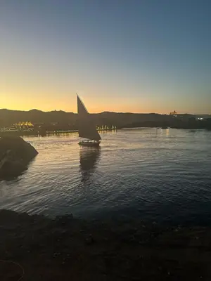 a small sail boat in the water at sunset at Nubia House Nile View in Nag` el-Ramla