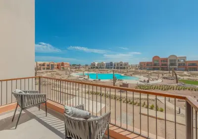a balcony with two chairs and a view of a pool at Sophisticated 1BR 1,5 Bath Duplex - Kamaran El Gouna, Pool View & Access in Hurghada
