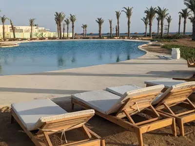 two lounge chairs and a swimming pool with palm trees at Somabay-Mesca - Relaxing Ground Floor in Hurghada