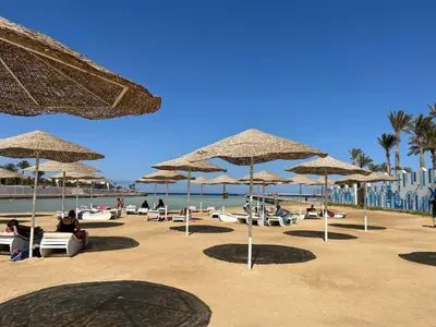 a beach with many straw umbrellas and people sitting at Scandic resort private beach in Hurghada