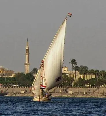 a sail boat in the water with a clock tower in the background at Lucky Nile Tours in Luxor