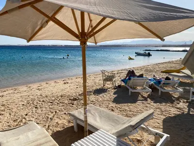 a beach with people sitting in chairs and an umbrella at Cozy studio in Azzurra Resort Sahl Hasheesh 65 Sq M in Hurghada