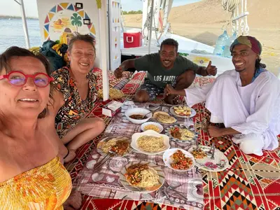 a group of people sitting around a table with food at Sunset and Sand Felucca Life on the Nile in Jazīrat Aswān