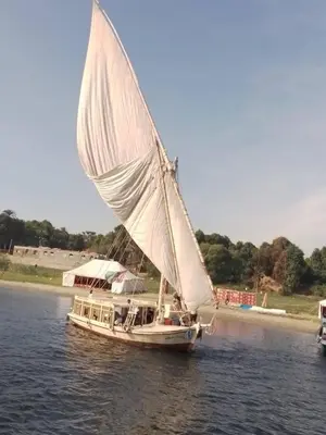 a boat with a white sail on the water at Sunset and Sand Felucca Life on the Nile in Jazīrat Aswān