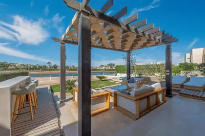 a wooden pergola on a patio with a pool at Serene Lakeview Escape 2BR at Cyan ElGouna in Hurghada