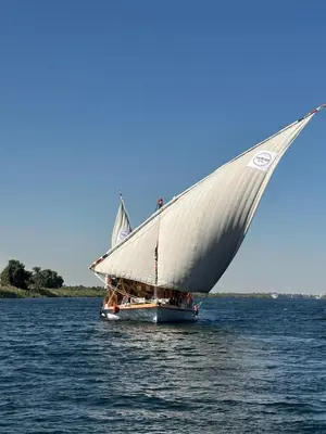 a boat with a large white sail on the water at Escaleeh Dahabiya Tranquil sailing in Jazīrat Suhayl