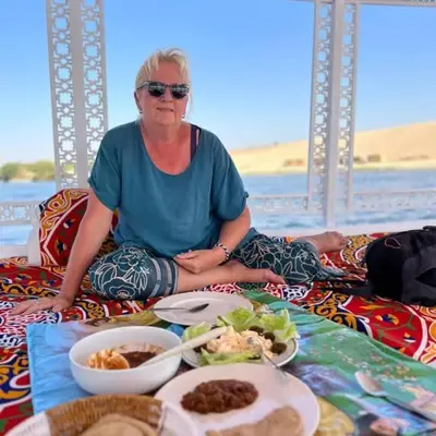 a woman sitting on a bed with a plate of food at Isis Nubian Services in Jazīrat Aswān