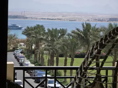 a balcony with palm trees and a boat in the water at Sea view Luxury apartment at Al Andalous Sahl Hasheesh in Hurghada