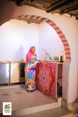 a woman standing next to a table in a kitchen at Heissa Nubian Hostel in Aswân Reservoir Colony
