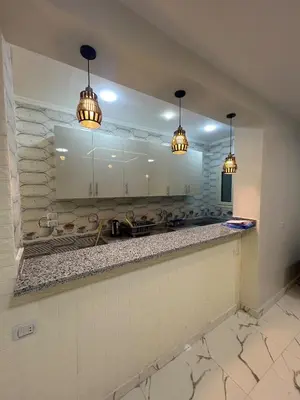 a kitchen with white cabinets and two pendant lights at Two Bedroom Apartment in Hurghada
