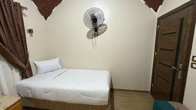 a bedroom with a bed and a fan on the wall at Lilys Garden Guest House in Jazīrat al ‘Awwāmīyah