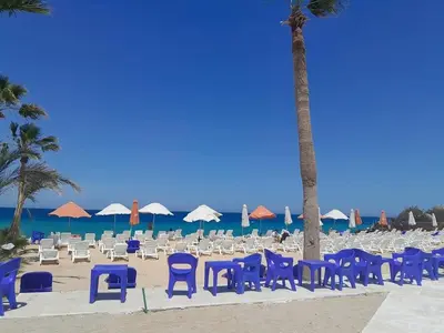 a group of chairs and palm trees on a beach at Stylish studio with sea view in Hurghada