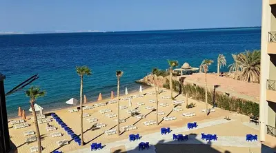 a beach with chairs and palm trees and the ocean at Stylish studio with sea view in Hurghada