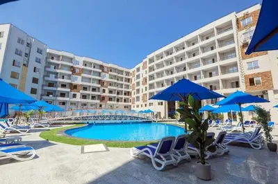 a swimming pool with chairs and blue umbrellas at Sami and Sam studio apartment in Hurghada