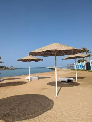 three umbrellas on a beach with chairs and the ocean at Private Garden Studio Wi-Fi and Beach Access in Hurghada