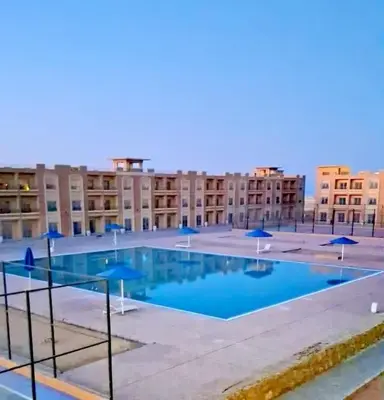 a large pool with blue umbrellas in front of a building at Sahl hashesh Resort in Hurghada